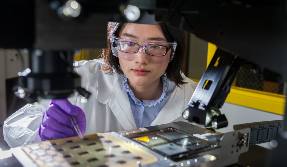 Image of an employee using a lab machine while wearing personal protective equipment